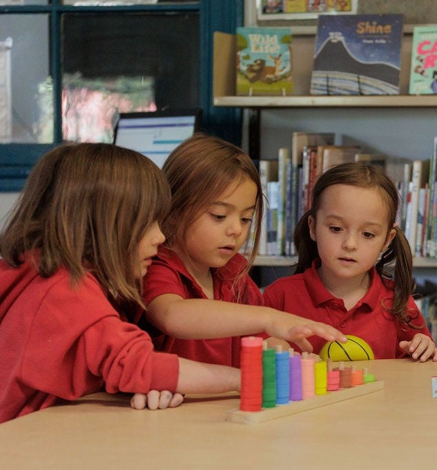 Image of three girls gathered around a table on which is colourful blocks arranged in descending order.