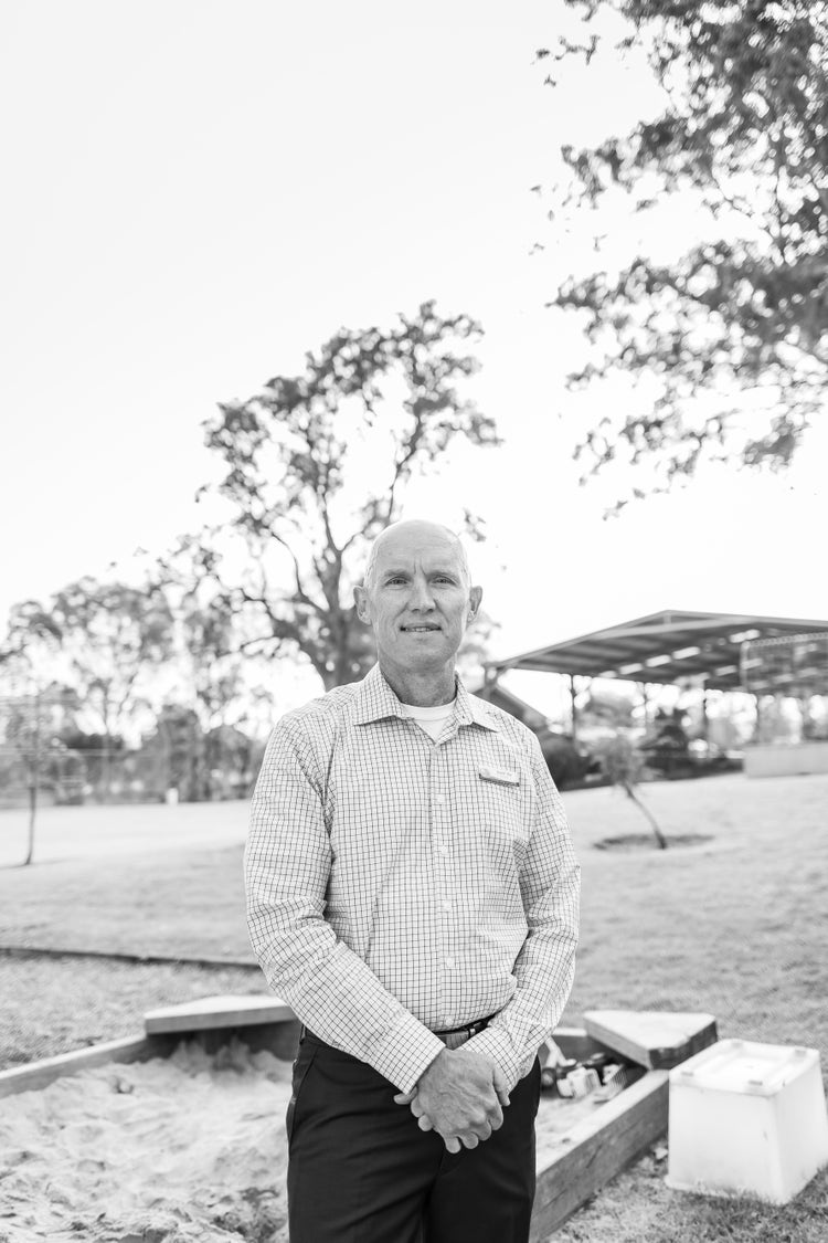 Image of Quaama Public School Prinicipal Daniel Roe standing in front of a sandpit and the school playground in the background.
