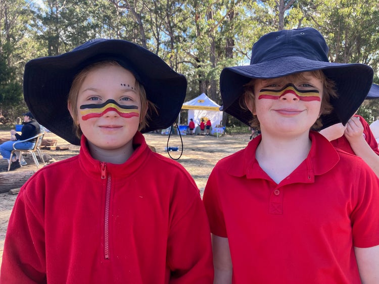 Image of a boy and girl student wearing school hats and face painted lines across their cheeks and the bridge of their noses in the aboriginal flag colours of black, red and yellow.