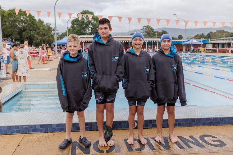 Students standing in front of a swimming pool with representative hoodies on.