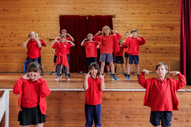 Students performing a dance on a stage and on the floor in front of the stage.